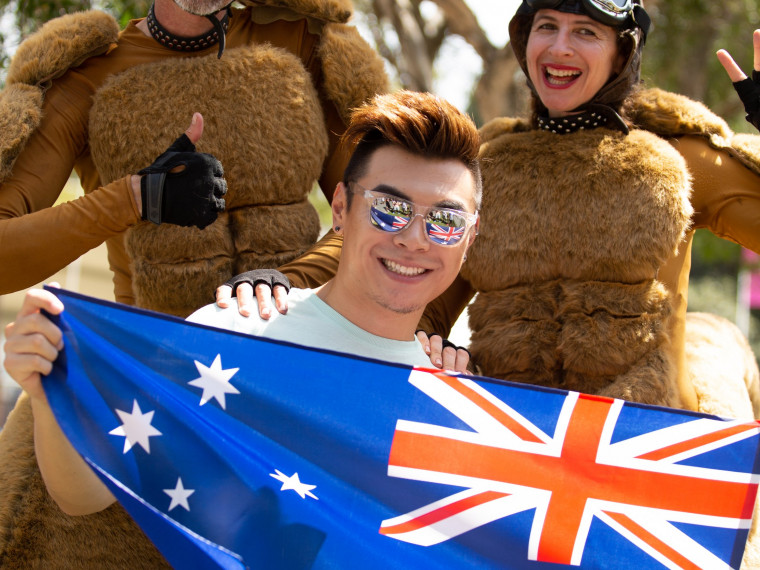 Happy man holding a flag and standing with giant bouncing roos at the Summer Playground in Darling Harbour