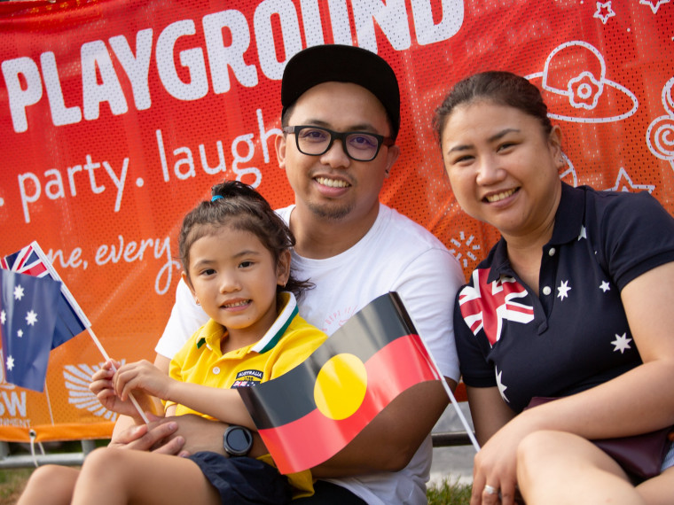 Young family holding Australian and Aboriginal flags at the Summer Playground in Darling Harbour
