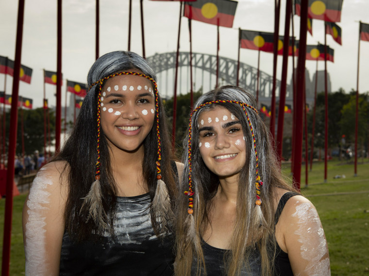 Performers at the WugulOra Morning Ceremony with Aboriginal flags and the Sydney Harbour Bridge